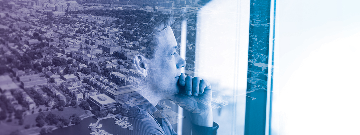 Profile of man looking out of a window, a city can be seen behind him