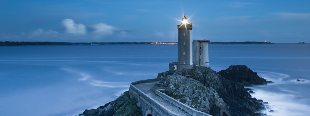Photo of a lit lighthouse at twilight.