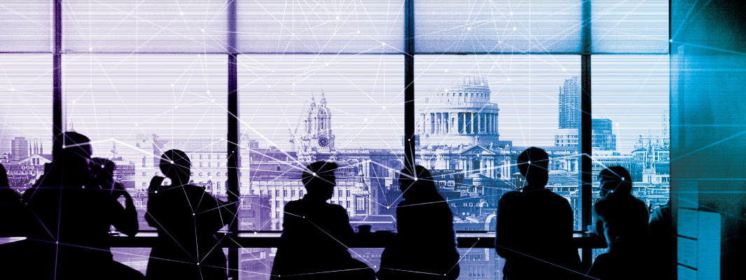 Photo of office buildings through a conference room window. Silhouetted business people are having a meeting in the room.